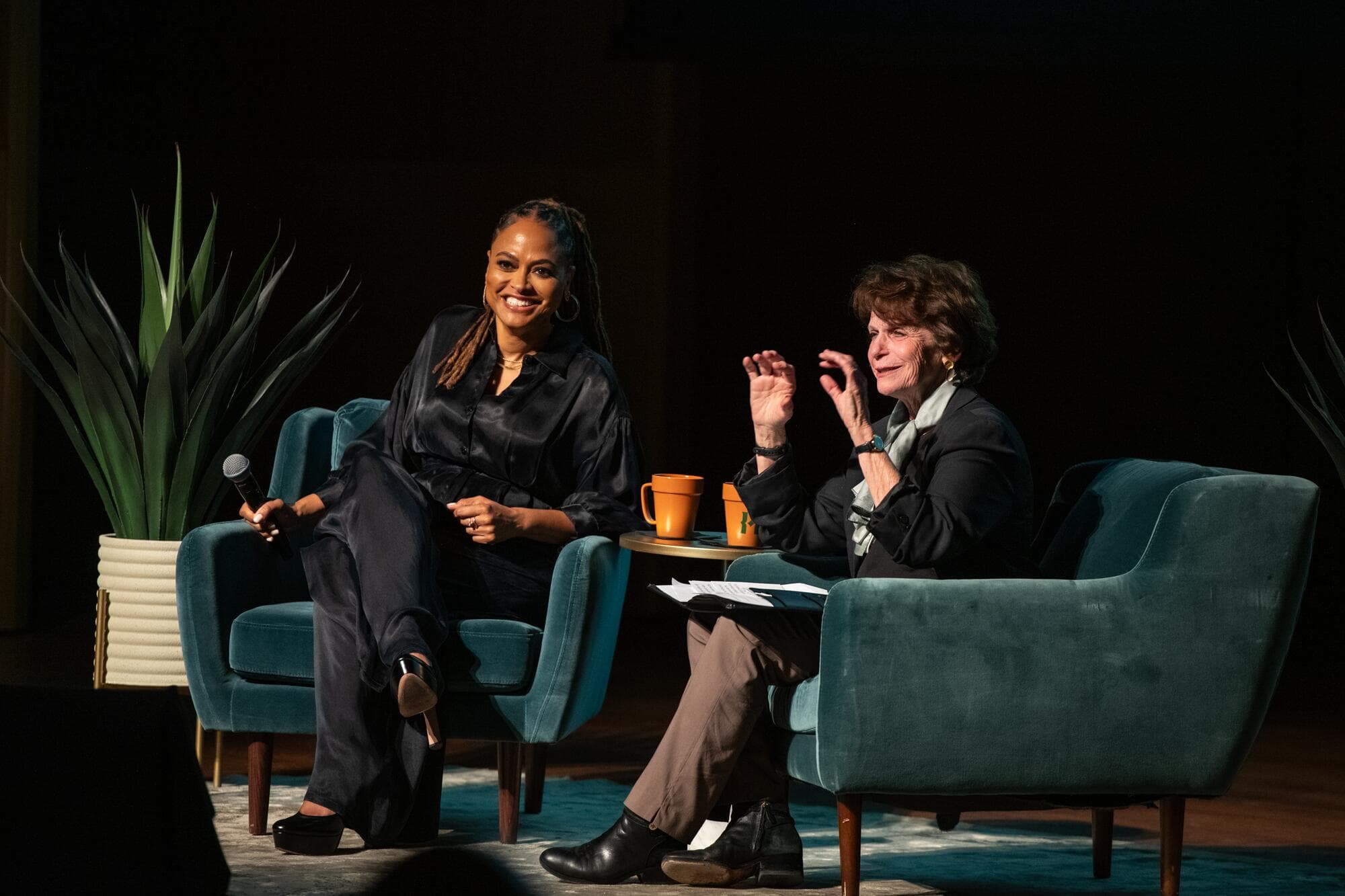 Two people, including famed filmmaker Ava DuVernay, sit in seats on a stage. 