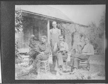 Five men outside posing for the picture with a dog sitting on a chair