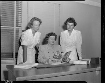 Three women looking at a cookbook for cooking electronically