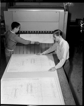 Prints of drawings coming off processing machine and being laid out on table