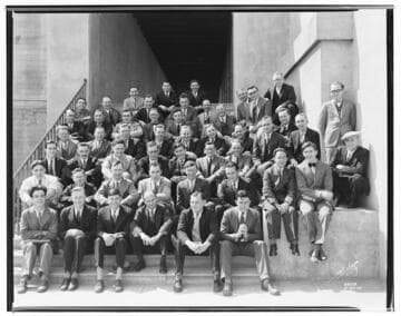Group shot of office workers in suits and ties sitting on steps of general office