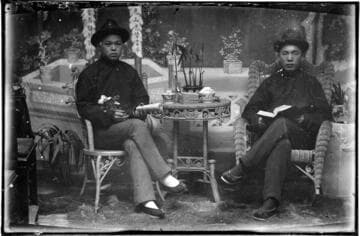 Portrait of two Chinese men seated on either side of a small table