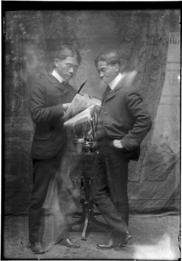 Portrait of two Chinese men, standing, looking at a newspaper