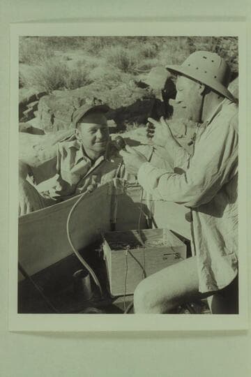 Red Carson gets instruction from Ed Hudson on the operation of the tape recorder carried in the "Esmeralda".  Carson flew in by helicopter to the beach at Hance Rapid to meet the motorboat party on June 15, 1950