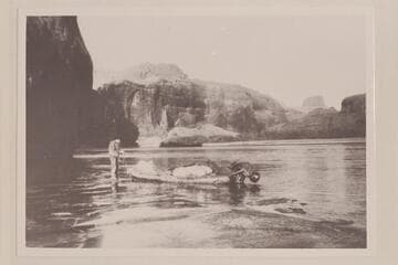 John Wetherill on the icy shore of Glen Canyon holding the painter of the outboard skiff used in a trip up to Rainbow Bridge and Hole in the Rock