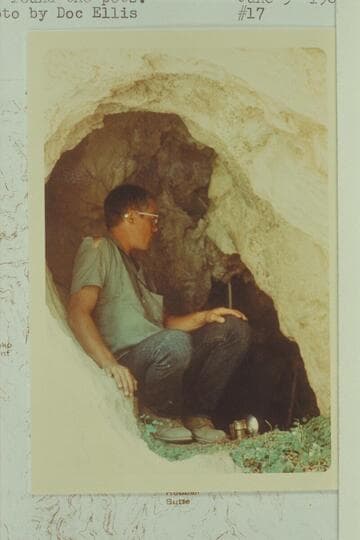 Don Davis crouched at entrance of cave in Lava Creek where he found pots