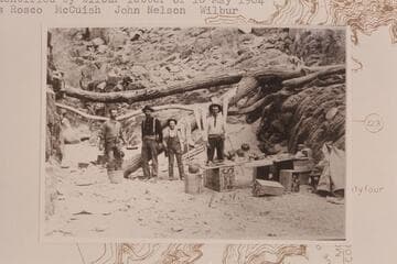 Prospecting party at breakfast probably at Diamond Creek.  Identified by Wilbur letter of 1904, May 10 as Rosco; McCuish; John Nelson; Wilbur