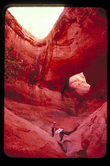 Masland and Marston holding Explorers Club flag at natural bridge in Navajo Canyon.  Masland proposes name, "Ba-Sah Bridge," for the seven pot-holes below it