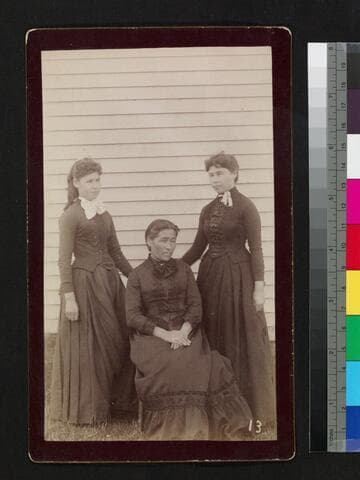 Three women, possibly native, in Caucasian dress, sitting in front of house