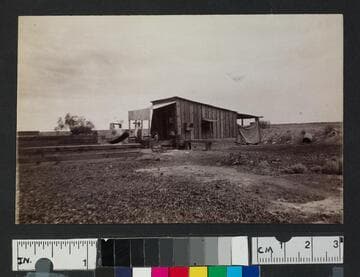 Man in front of wooden house in unidentified settlement