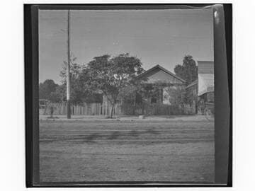Unidentified house on city street with a harness shop at right