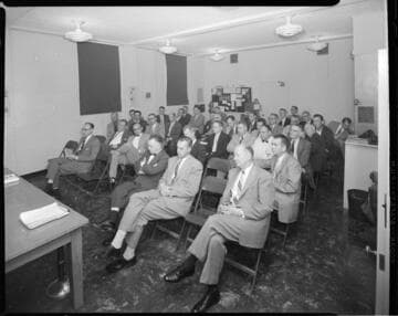 Staff meeting with 16mm projector set-up for movie presentation