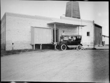 Public ice house with customer purchasing a block of ice at the loading dock in his touring car
