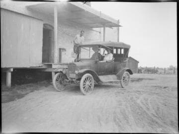 Customers buying a block of ice at the loading dock of the local ice house in their Model A touring car