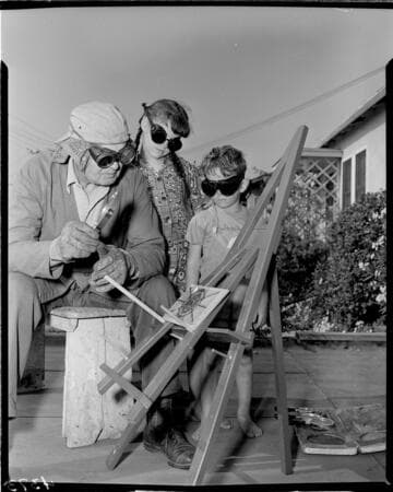Man working with his hobby is burning patterns on wood with a magnifying glass; two children are watching