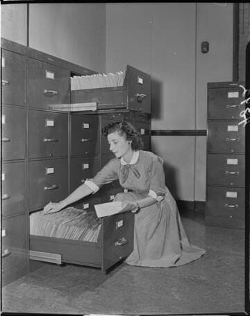 Lady filing paper in bottom file while file drawer just above her head is open
