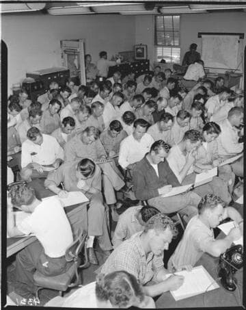 Room full of men filling out "Personnel Survey" forms