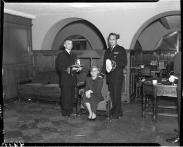 Woman seated with two men in uniform standing by