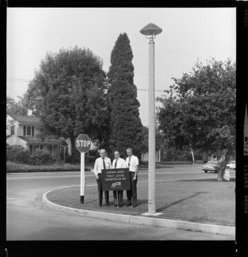 Men by streetlight on street corner with sign "Chapman Woods Street Lighting Demonstration Unit."