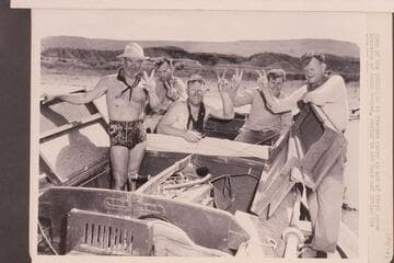 Crew of the "Esmeralda" at Pierces Ferry at end of first motor traverse of Grand Canyon, posing in the boat and giving the victory sign.  Left to right:  Marston, Robinson, Ed Hudson, Edward Hudson and Taylor