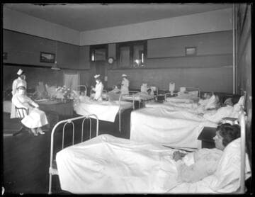 Patients in hospital beds being tended to by nurses. 1919?