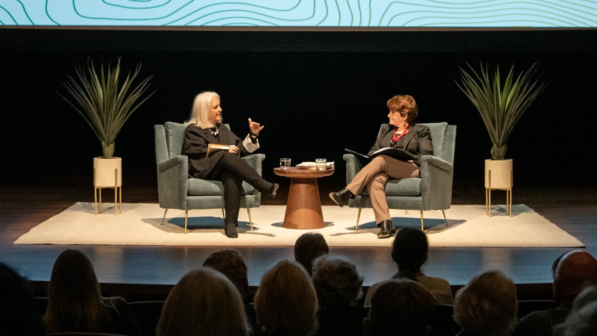 Two people sit on stage in front of an audience.